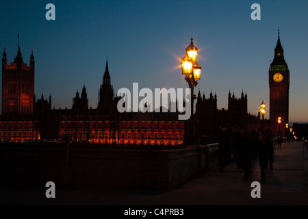 Eine untergehende Sonne Silhouetten der Houses of Parliament und Big Ben in London, England. Verwischte die Menschen gehen über die Brücke. Stockfoto