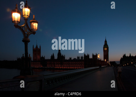 Eine untergehende Sonne Silhouetten der Houses of Parliament und Big Ben in London, England. Auf der Brücke leuchten hell. Stockfoto