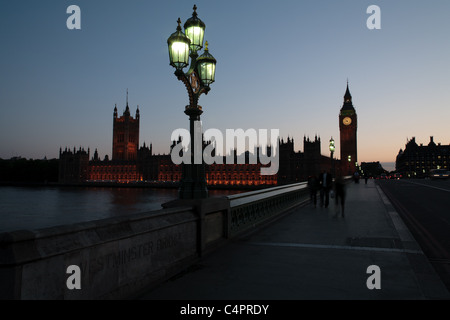 Eine untergehende Sonne Silhouetten der Houses of Parliament und Big Ben in London, England. Verwischte die Menschen gehen über die Brücke. Stockfoto