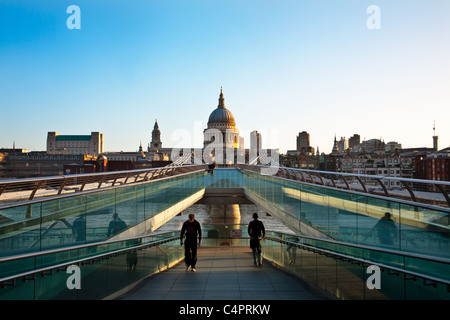 Früh am Morgen Sonne erhellt St. Pauls an der Spitze der Millennium Bridge. Zwei Menschen spiegeln sich in den Glasscheiben. Stockfoto