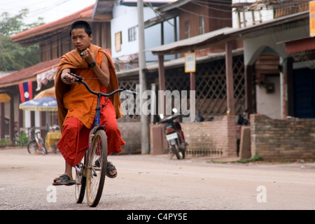 Ein junger Mönch reitet ein Fahrrad auf einer unbefestigten Straße in ländlichen kommunistische Laos. Stockfoto