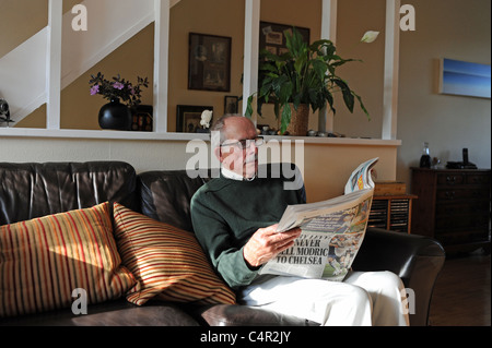 Mann Mitte der Achtziger, der am Sonntag eine nationale Zeitung The Mail auf einem Sofa im Wohnzimmer in Großbritannien las Stockfoto