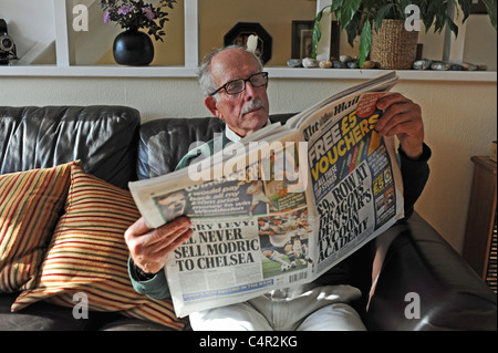 Mann Mitte der Achtziger, der am Sonntag eine nationale Zeitung The Mail auf einem Sofa im Wohnzimmer in Großbritannien las Stockfoto