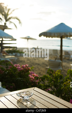 Aschenbecher am Tisch am Strand, Sonnenschirme und Liegestühle im Hintergrund Stockfoto