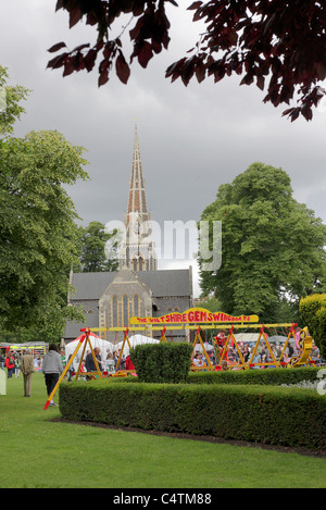 Die für Spaß in der Messe an öffentlichen Turnham Green Park, junge Kinder genießen die Schaukeln vor dem Hintergrund der lokalen Kirche. Stockfoto