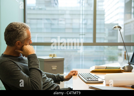 Mann am Schreibtisch im Büro, in Gedanken wegschauen Stockfoto