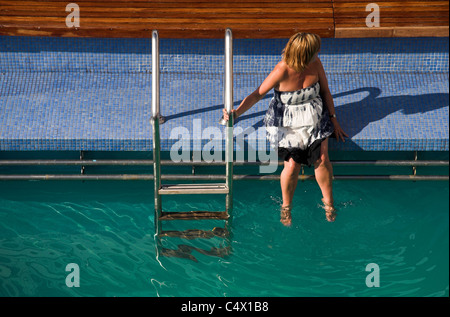 Frau sitzt vom Beckenrand von dem Lido-Deck eines Kreuzfahrtschiffes Stockfoto