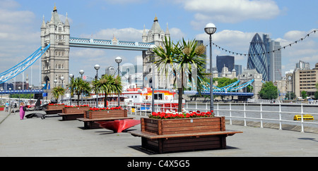 Thames Path an der Butlers Wharf Promenade mit Blick auf die Themse Tower Bridge und die Londoner Skyline rote Blumen Reihe von Pflanzkästen cordyline Trees London UK Stockfoto