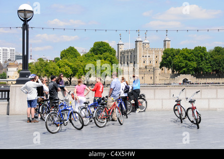 Eine Gruppe von Touristen, die bei einer begleiteten Besichtigungstour Fahrräder ausgeliehen haben und dem Reiseleiter (in rot) gegenüber dem Tower of London neben der Themse England zuhören Stockfoto