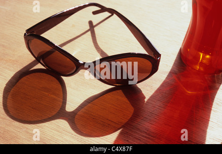 Sonnenbrillen und roten Becher auf Holz-gekörnt Tischplatte und farbige Schatten Stockfoto