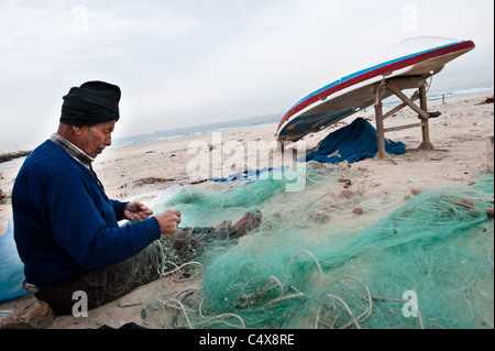 Ein älteren palästinensischen Fischer flickt seine Netze am Strand von Gaza-Stadt. Stockfoto