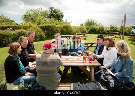 Eine Gruppe von Leuten, die draußen sitzen und im Biergarten des Jolly Sailor Pub, Orford, Suffolk, Großbritannien, trinken Stockfoto
