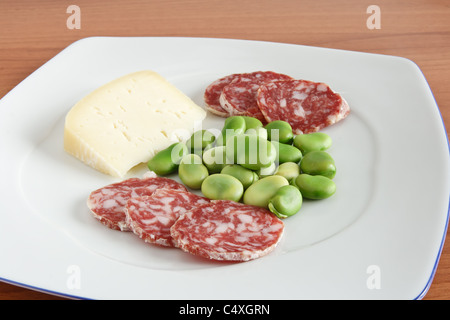 Dicke Bohnen mit Pecorino-Käse und Salami-Scheiben auf einem weißen Teller Stockfoto