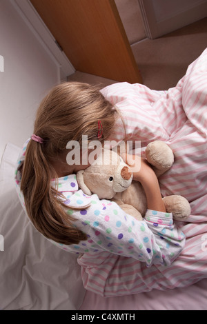 Junges Mädchen kuscheln einen Teddybär sitzt auf dem Bett, Kopf nach unten. Stockfoto