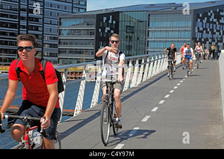 Fröhliche Jungen oder Jugendliche auf Rädern, die die 190 m lange und 5,5 m breite Rad- und Fußgängerstahlbrücke über den Hafen von Kopenhagen, Dänemark, passieren. Stockfoto