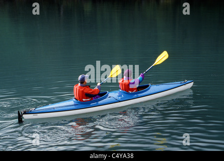 Zwei Besucher in bunten Jacken und Schwimmwesten Paddel im Einklang mit dem Kajak in Takatz Bay aus Baranof Island entlang der Inside Passage in Alaska, USA. Stockfoto