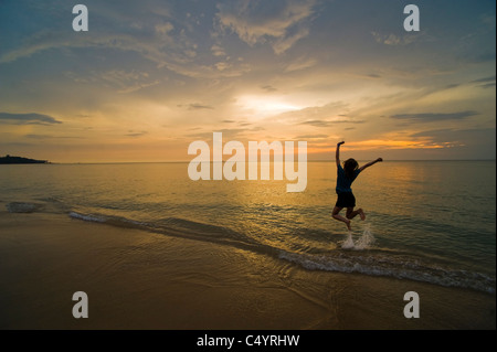 Eine junge Frau springen vor Freude und feiern am Strand bei Sonnenuntergang. Aufgenommen am Phra Ae Beach, Koh Lanta, Süd-Thailand