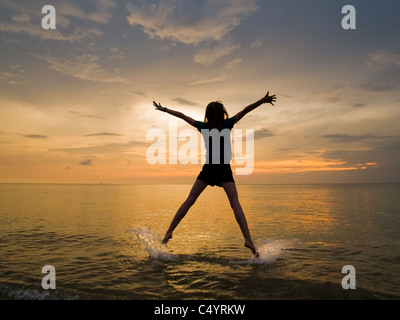 Eine junge Frau tut ein Stern springen, springen vor Freude und genießen ihre Freiheit am Strand bei Sonnenuntergang.