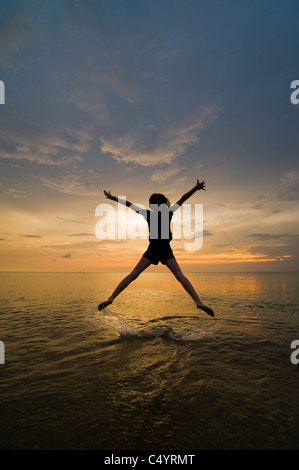 Eine junge Frau tut ein Stern springen, springen vor Freude und genießen ihre Freiheit am Strand bei Sonnenuntergang.
