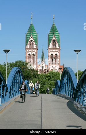 Radfahrer, die die Blaue Brücke überqueren, eine Rad-/Fußgängerroute über Bahnstrecken, Freiburg, Deutschland. Die Herz Jesu Kirche dahinter. Stockfoto