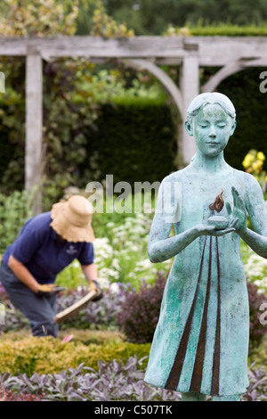 Eine Statue von einer schönen Frau in einem Garten mit einer weiblichen Gärtner, die Pflege der Gärten Stockfoto