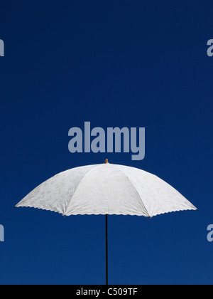 Ein Hand gehaltenen weißen Leinen Sonnenschirm mit gestickten Details, legen Sie gegen einen klaren, blauen Sommerhimmel. (Querformat Ref C509TX) Stockfoto