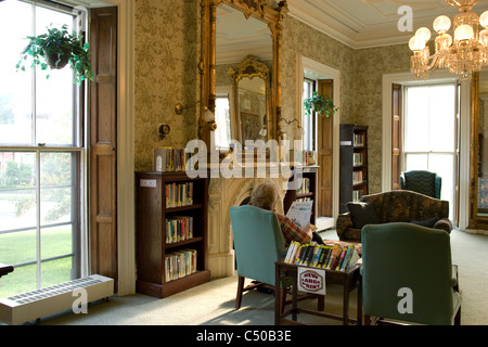 Ein Gönner sitzt in einer komfortablen öffentlichen Bibliothek Lesesaal.  Beachten Sie die Zeichen für große vergriffene Bücher. Stockfoto