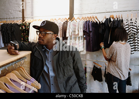 Afrikanische amerikanische Mann SMS auf Handy in Bekleidungsgeschäft Stockfoto