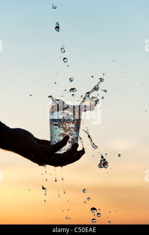 Wasser wird bei Sonnenuntergang in einem Plastikbecher gegossen. Silhouette. Indien Stockfoto