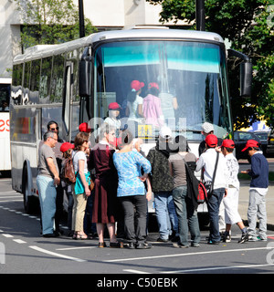 Fahrer und Lehrer beaufsichtigen das Einsteigen der Schüler in den Linkslenker. Ausländischer Bus mit viel Verkehr passiert die Einfahrt zur Parkbucht Park Lane London England UK Stockfoto