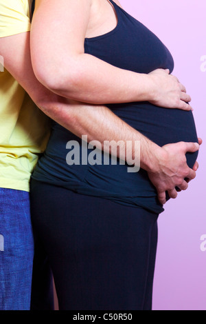 Foto von einer schwangeren Frau mit ihrem Ehemann hinter beiden mit ihren Händen auf dem Bauch Stockfoto