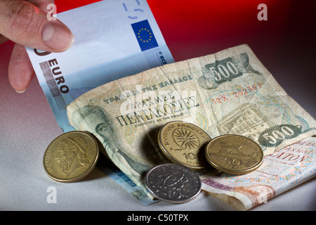 Eine Hand, die ein-Euro-Schein unter einem Haufen von griechische Drachmen herausziehen: mit der neuen mit den alten. Stockfoto