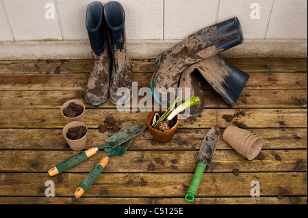 Schlammigen Stiefel und Gartengeräten auf Rückseite deck mit Blumentöpfe mit Hyazinthe Birne im Topf nach der Arbeit im Garten. Stockfoto