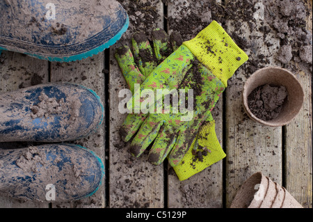 Gartenarbeit-Töpfe mit schlammigen Stiefeln auf einem deck mit Arbeitshandschuhen Stockfoto