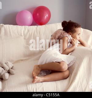 Kleines Mädchen auf der Couch liegend mit Stofftier in der hand lächelnd Stockfoto