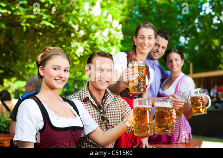 Im Biergarten - Freunde in Tracht, Dirndl und Lederhosen ein frisches Bier in Bayern, Deutschland Stockfoto