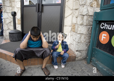 Bruder sitzt mit kleinen Schwester warten auf Mama im Store auf Kirche Avenue im Kensington Viertel, Brooklyn, NY Stockfoto