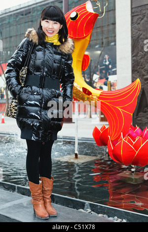 Junge asiatische Frau stehen in der Nähe einen Brunnen mit Fisch Dekoration und lächelnd, Xian, China Stockfoto