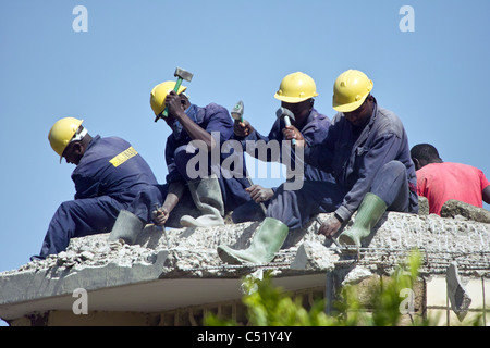 Arbeiter sitzen auf Dach aufbrechen Beton mit Club-Hämmer Stockfoto