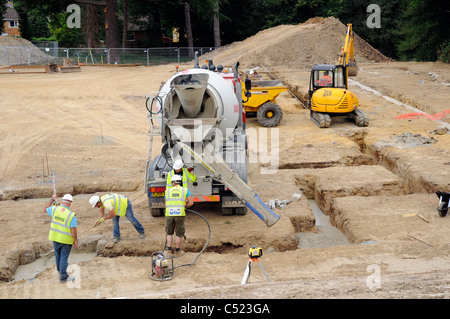 Baustelle zeigt Streifen Stiftung Gräben und Betonmischer liefern konkrete und Vermesser prüfen Tiefe. Stockfoto