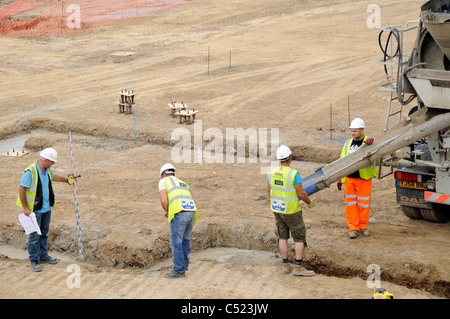 Baustelle zeigt Streifen Stiftung Gräben und Betonmischer liefern konkrete und Vermesser prüfen Tiefe. Stockfoto