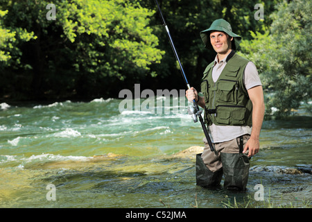 Ein junger Fischer posiert mit Angelrute in der Hand auf einem Fluss Stockfoto