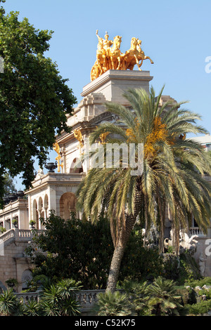 Die Barcelona Quadriga de le Aurora mit einem goldenen Wagen auf eine höchst architektonischen Gebäude mit Palmen vor. Stockfoto