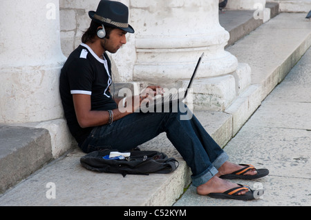 Junger Mann mit einem Notebookcomputer auf den Stufen eines öffentlichen Gebäudes in Vicenza, Italien Stockfoto