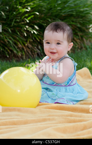 Ein acht Monate altes kaukasische Mädchen lacht während des Spiels mit einem gelben Ball im Freien. Stockfoto