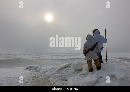 Inupiaq Eskimo Jäger in Parkas tragen ein Gewehr und Spazierstock während der Blick über die Tschuktschensee, Barrow, Alaska Stockfoto