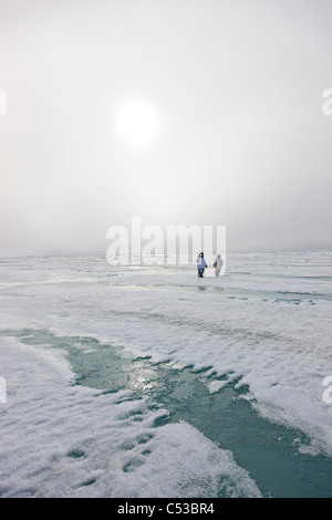 Inupiaq Eskimo Jäger tragen ein Gewehr und Gehstock bei einem Spaziergang über das Ufer Eis entlang der Tschuktschensee, Barrow, Alaska Stockfoto