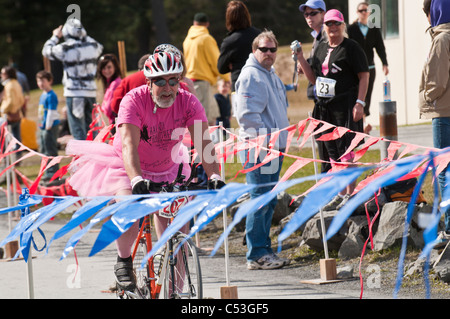 Mann gekleidet in ein rosa Hemd und Tutu Kostüm Fahrräder über die Ziellinie in rosa Wangen Triathlon, Seward, Alaska Stockfoto