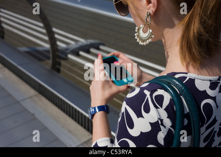 Eine junge Frau herüber der Millennium Bridge in London, wobei ihr Smartfone. Stockfoto