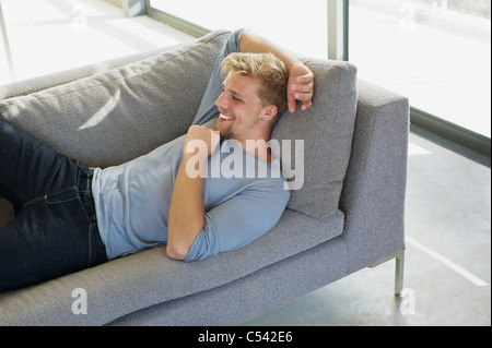 Erhöhte Ansicht eines jungen Mannes auf einer Couch zu Hause liegen und lächelnd Stockfoto